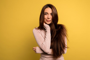 tender beautiful girl with dark hair wearing pink shirt posing over yellow background. Studio shot of blissful brunette woman