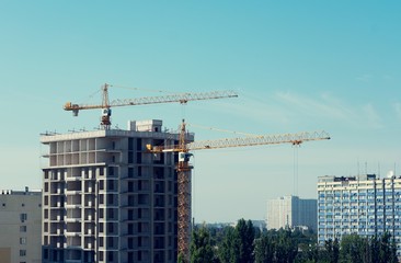 Fototapeta premium Construction of an apartment building, building cranes, blue sky with fluffy clouds, toned