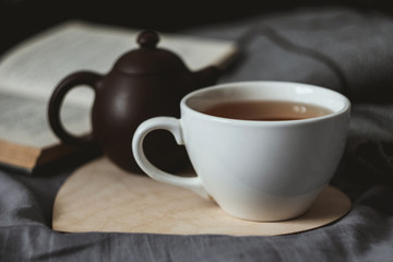 Cup of tean and teapot on wooden heart book and scarf on background