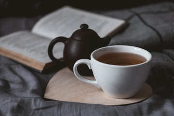 Cup of tean and teapot on wooden heart book and scarf on background