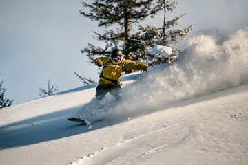 Snowboarder in a yellow jacket slides down a mountain slope