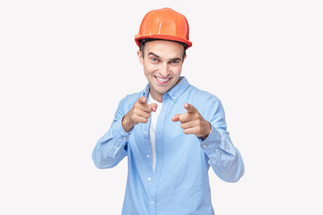 Joyful builder in helmet indicates fingers at you, isolated background, copy space