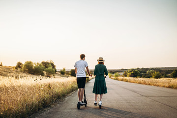 Fototapeta premium Young couple on vacation having fun driving electric scooter on the road in the countryside. Content technologies. Back view