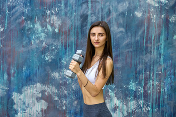 Fototapeta premium Happy young woman with dumbbells making exercises outdoors in front of modern painted wall