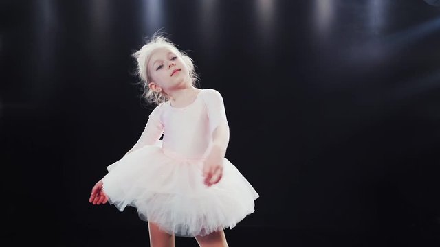 Little girl ballerina Caucasian appearance in a white tutu dances on stage. Children. Slow motion