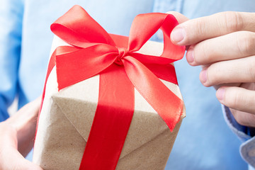 Man holding gift with red ribbon, man's hands, closeup