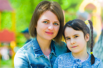 Summer portrait of mom and daughter in the park. On the background of blurry children's slides