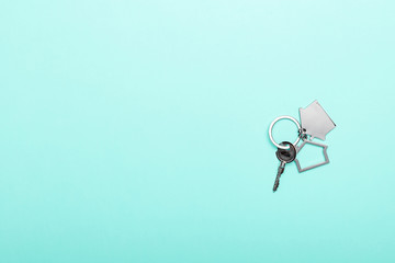 House keys with trinket on color background, top view with copy space. House key on blue background. Minimal flat lay style with place for text.
