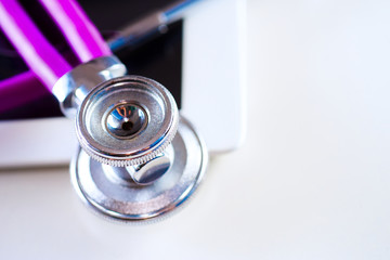 Medical equipment: purple stethoscope and tablet on white background