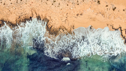 Aerial top view of sea waves with foam on wild sandy beach in Cyprus.