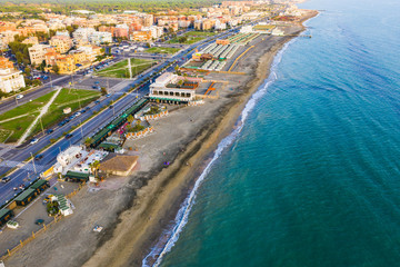 Ostia Lido beach in Italy in warm autumn evening, sandy coast, road near beach and buildings, aerial view.