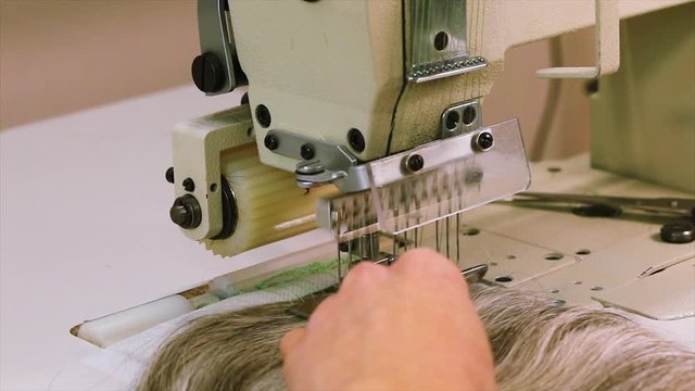 Woman sews hair to the base of the wig