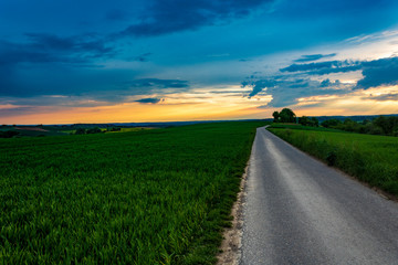 Fototapeta na wymiar country road in the field against blue sunset sky in Neudenau, Germany.