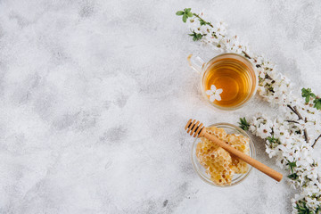 Spring composition. A cup of herbal tea and a jar of honey on a grey beton background, cherry...