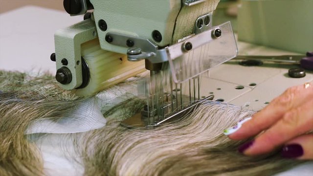 Sewing a wig on a sewing machine, a woman produces a wig