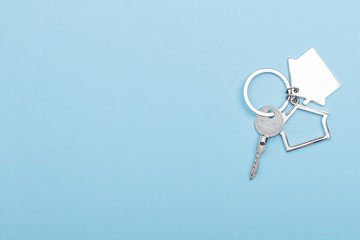 House keys with trinket on color background, top view with copy space. House key on blue background. Minimal flat lay style with place for text.