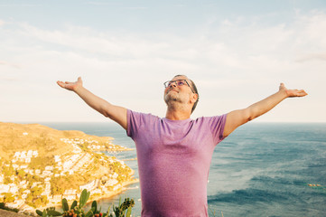 Summer portrait of middle age man posing by the sea, arms wide open, top view