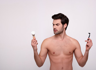 A beautiful naked man holds a razor and a shaving anoint.