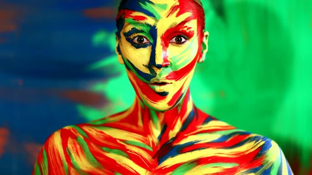 Color face art and body paint on woman for inspiration. Abstract portrait of the bright beautiful girl with colorful make-up and bodyart. Cheerful woman showing wow emotion.