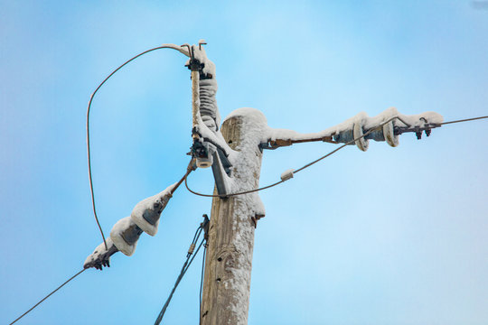 Street furniture and urban infrastructure enduring a harsh winter as a utility pole with overhead electricity cables is seen close up covered in snow