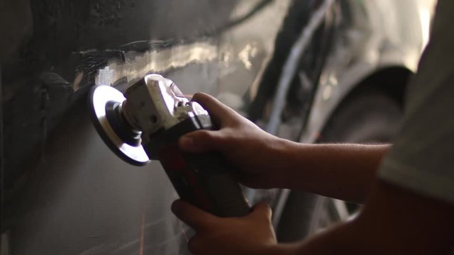  man hand works on the sheet and paint of a car with grinder