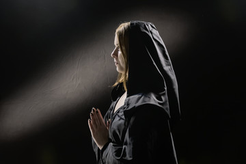 Portrait of a young girl 25-30 years old in monastic clothes, a woman praying with folded hands, a symbol of faith and hope, sunlight