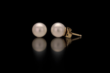 A close up of a pair of white pearl earring studs with yellow gold post and nut on a black...