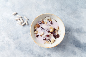 Bowl of granola with yogurt, nuts, cranberry and cocoanut. Sport supplements ( carnitine capsules ) in background. Bright stone  background. Top view. Copy space. 