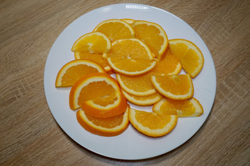 Bright slices of ripe juicy orange on a white plate on a wooden table in the kitchen