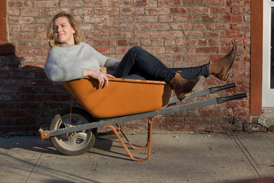 caucasian millennial female business owner in wheelbarrow in grey turtleneck in brooklyn smiling