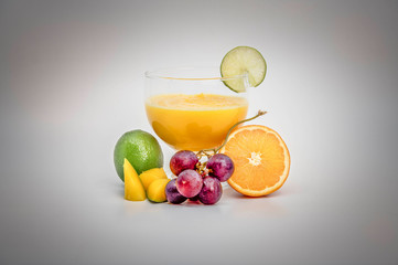 Orange juice in a big glass, fruits arount glass, lime slice on glass margin