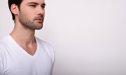 The cropped frame, a handsome white man in a white T-shirt looks to the side.