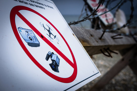 no photo, video or drones allowed sign with red circle in restricted by the beach with wired fence on the background. NO go zone.