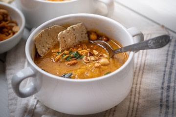 Vegan pumkin and spice soup garnished with peanuts and crackers on white wooden table
