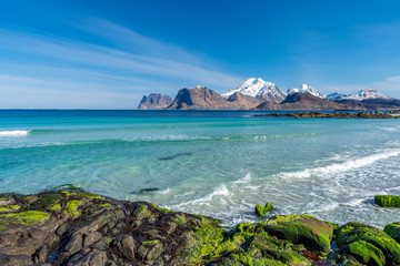 Empty beautiful beach during springtime on a sunny day with blue sky and silent ocean with small waves. Mountain chain with snow in the background. From Myrland beach in Lofoten - Norway. 