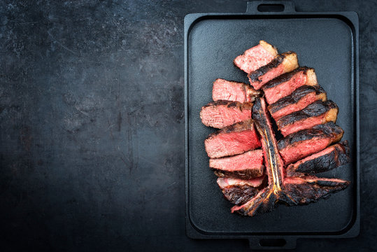Barbecue dry aged wagyu porterhouse beef steak sliced with large fillet piece as top view on a modern design black cast iron tray with copy space left
