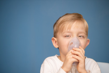 A strabismus boy doing inhalation with a nebulizer on a blue background.