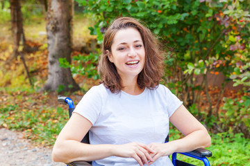 Naklejka na ściany i meble Young happy handicap woman in wheelchair on road in hospital park waiting for patient services. Paralyzed girl in invalid chair for disabled people outdoor in nature. Rehabilitation concept.