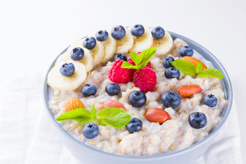 Healthy breakfast. Oatmeal with blueberries, banana and raspberry. Oatmeal with fruits and nuts in a bowl. Cooked oatmeal on white background. Vegetarian food. Copy space