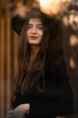 Fototapeta premium Outdoor photo of brunette lady posing on tree background in autumn day.Fashion street style portrait.Girl wearing dark casual clothes and dark hat .Fashion concept.