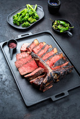 Barbecue dry aged wagyu porterhouse beef steak sliced with large fillet piece with hot chili and rapini broccoli rabe as closeup on a modern design black cast iron tray