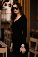 Photo of brunette lady posing on wooden background in cafe.Fashion style portrait. Girl wearing dark casual dress, sunglasses and dark hat .Fashion concept.