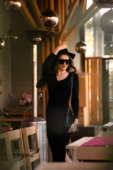 Photo of brunette lady posing on wooden background in cafe.Fashion style portrait. Girl wearing dark casual dress, sunglasses and dark hat .Fashion concept.