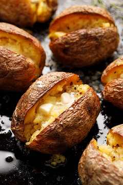 Baked potato, hot baked potatoes with the addition of butter and freshly ground black pepper and sea salt flakes on a black background, close up