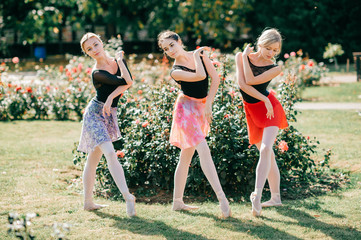 Three beautiful ballerinas girls dancing and balancing over sun light in summer park with beautiful background