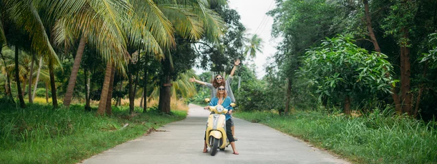Fotobehang A pair of beautiful women travel by scooter through the jungle in Southeast Asia. Thailand © Anna