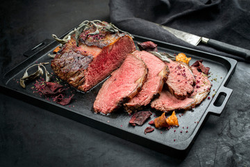 Traditional Commonwealth Sunday roast with sliced cold cuts roast beef with vegetable chips and herbs as closeup on a modern design tray