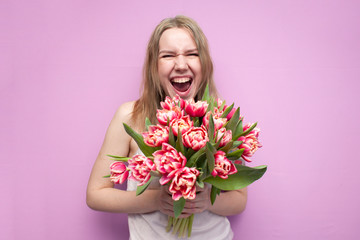 young beautiful girl with a bouquet of flowers on a colored pink background, a woman holds tulips and screams from happiness