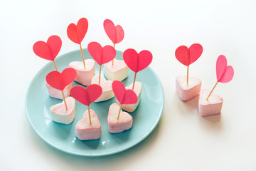 Marshmallows and paper hearts on skewers stuck in meringues standing on a blue turquoise mint...