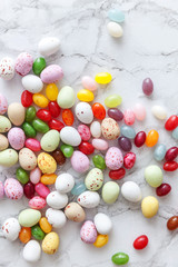 Happy Easter concept. Preparation for holiday. Easter candy chocolate eggs and jellybean sweets on trendy gray marble background. Simple minimalism flat lay top view copy space.